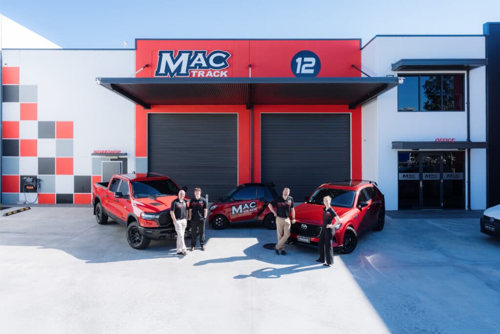 MacTrack team members standing with company vehicles outside their headquarters building.